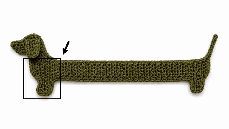 Crochet dachshund bookmark handmade with yarn, featuring a long body, short legs, floppy ear, and curly tail.